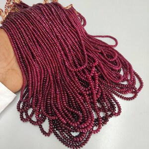 Puede incluir: Una hebra de cuentas de rubí rojo oscuro, ensartadas para formar un collar largo. Las cuentas son pequeñas y redondas, y están dispuestas en una fila ordenada y uniforme.