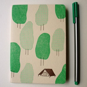May include: A cream-coloured notebook cover with a green and white pattern of trees and a small tent. The cover has a textured surface.