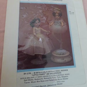 May include: A package showing two ballerina dolls, one in a white dress and the other in a tutu. The package includes text that reads "Byron Doll Patterns" and "Little Fairy as Ballerinas". The dolls are displayed on a decorative base.