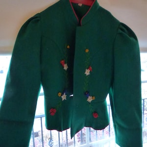 May include: A green jacket with a red trim and collar. The jacket features embroidered floral designs in various colors, including red, white, yellow, and blue. The sleeves are long and slightly puffed at the shoulders. The jacket is open in the front.