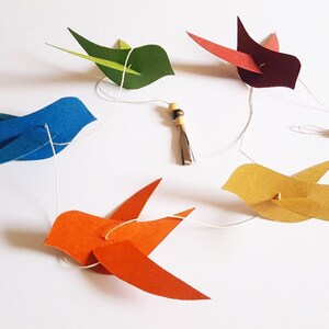 Guirlande d’oiseaux colorés en papier suspendus sur un fil blanc, avec perles en bois.