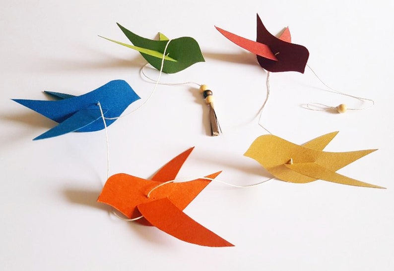 Guirlande d’oiseaux colorés en papier suspendus sur un fil blanc, avec perles en bois.