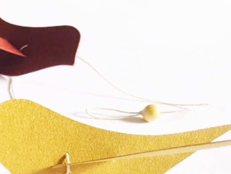 Guirlande décorative faite main avec cinq oiseaux découpés en papier recyclé aux teintes bleu, vert, rouge, jaune moutarde et orange, fixés sur un fil de coton avec perles de bois et un pompon en papier.