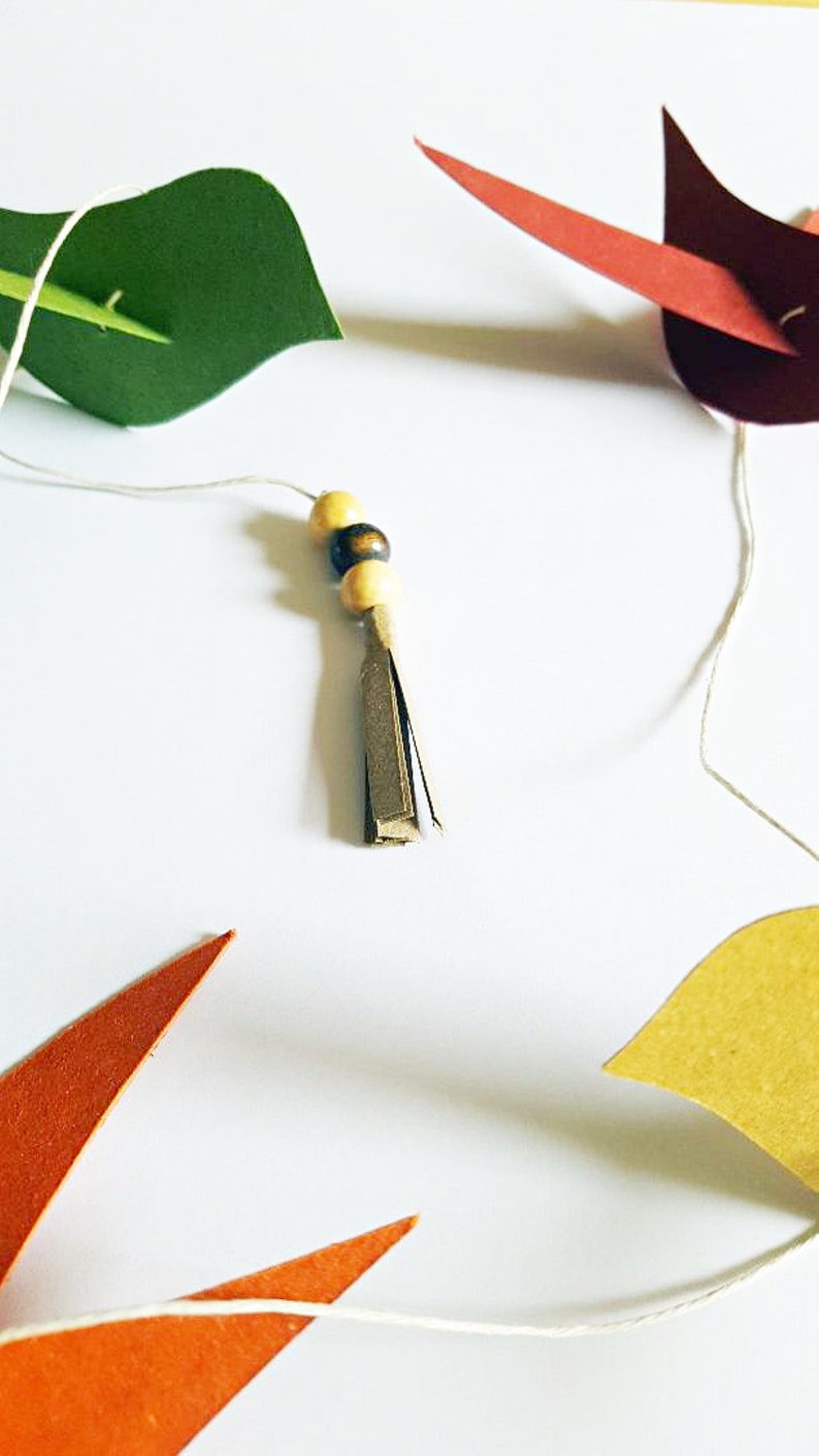 Guirlande d’oiseaux colorés en papier recyclé faits main, suspendus sur un fil blanc.
