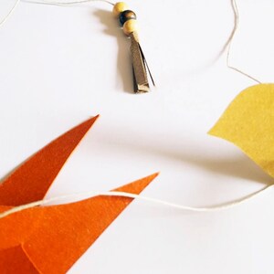Guirlande légère composée de cinq oiseaux en papier recyclé aux couleurs vives, comme suspendus dans les airs, apportant une touche de poésie et de douceur à toute décoration murale.
