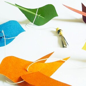Guirlande joyeuse avec de petits oiseaux colorés en papier recyclé, parfaite pour une chambre d’enfant ou un coin lecture doux et ludique.
