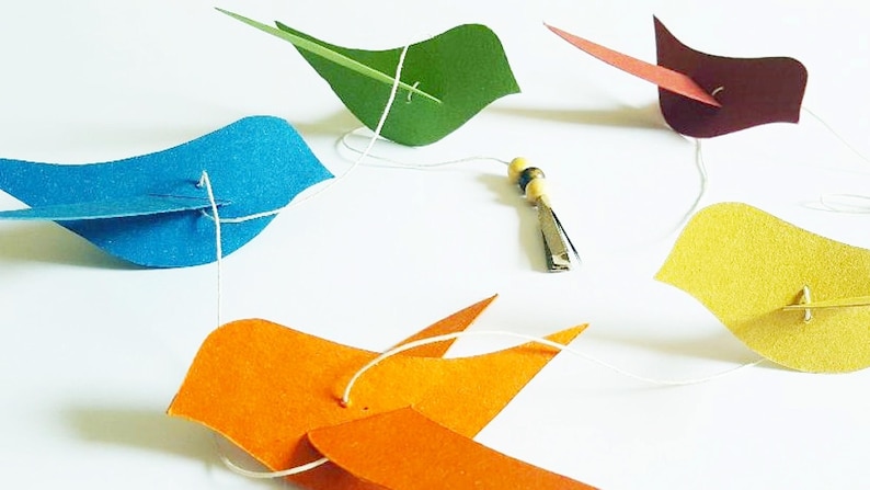 Guirlande joyeuse avec de petits oiseaux colorés en papier recyclé, parfaite pour une chambre d’enfant ou un coin lecture doux et ludique.