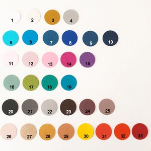 May include: A collection of thirty-three circular felt swatches arranged in rows, each labelled with a black number from 1 to 33. The swatches display a wide spectrum of colours including white, yellow, grey, blue, pink, purple, green, brown, and red.