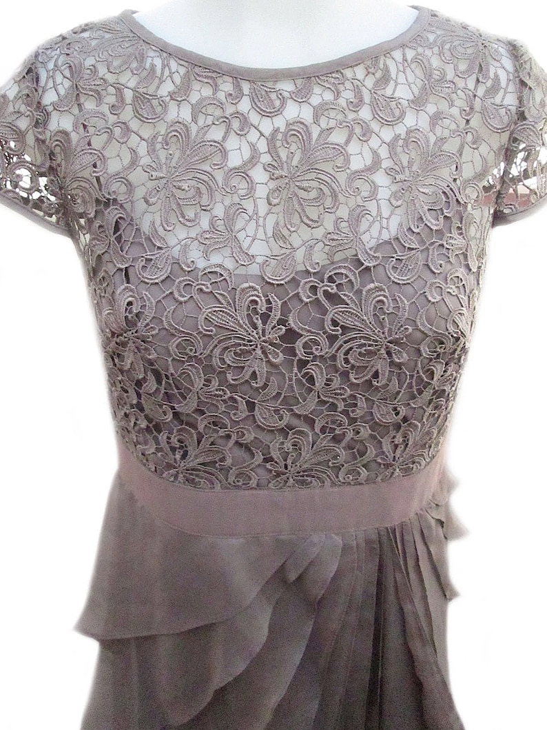May include: A gray lace dress with a ruffled skirt. The dress has a round neckline and short sleeves.