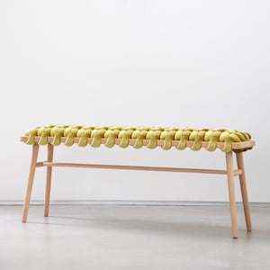 Puede incluir: Un banco de madera con un asiento de terciopelo verde tejido. El banco tiene un diseño sencillo con cuatro patas y una parte superior recta.