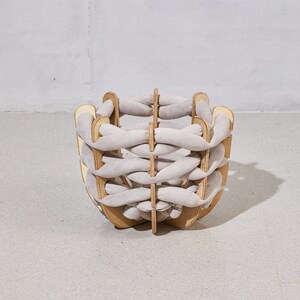 Pode incluir: Uma cadeira contempor&acirc;nea com design de cesta. A cadeira apresenta um padr&atilde;o tecido cinza claro, sustentado por uma estrutura de madeira castanho claro. O design &eacute; pr&aacute;tico e decorativo, adequado para v&aacute;rios interiores.