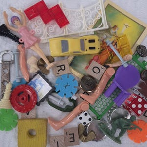 May include: A collection of small toys and game pieces, including a yellow toy car, a ballerina figurine in a pink dress, Scrabble tiles, dice, and a toy soldier. Various colors and shapes are present.