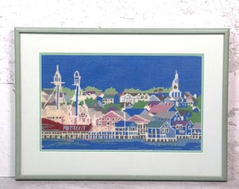 May include: A framed cross-stitch embroidery depicting a coastal town scene with a large ship docked at a pier, colourful houses, and a church steeple against a deep blue sky. The artwork is enclosed in a light green frame with a matching mat border.