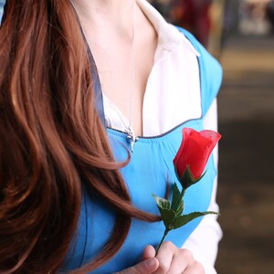 May include: A woman wearing a blue dress with a white collar and a red rose in her hand.