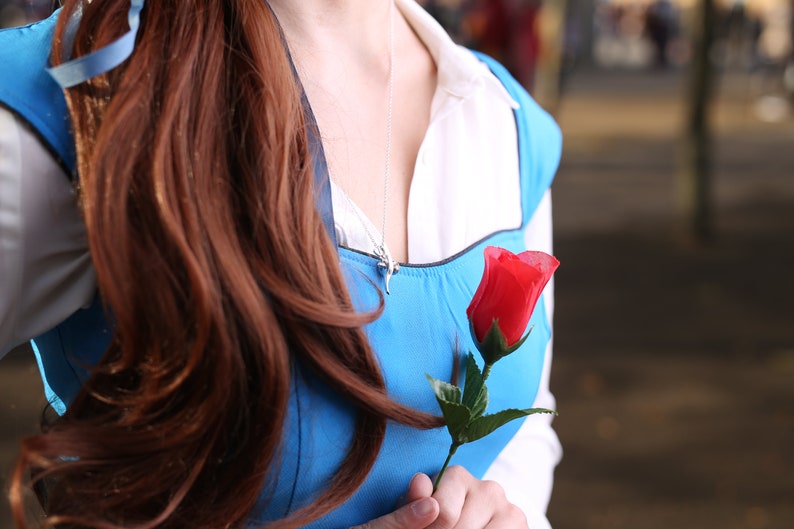 May include: A woman wearing a blue dress with a white collar and a red rose in her hand.