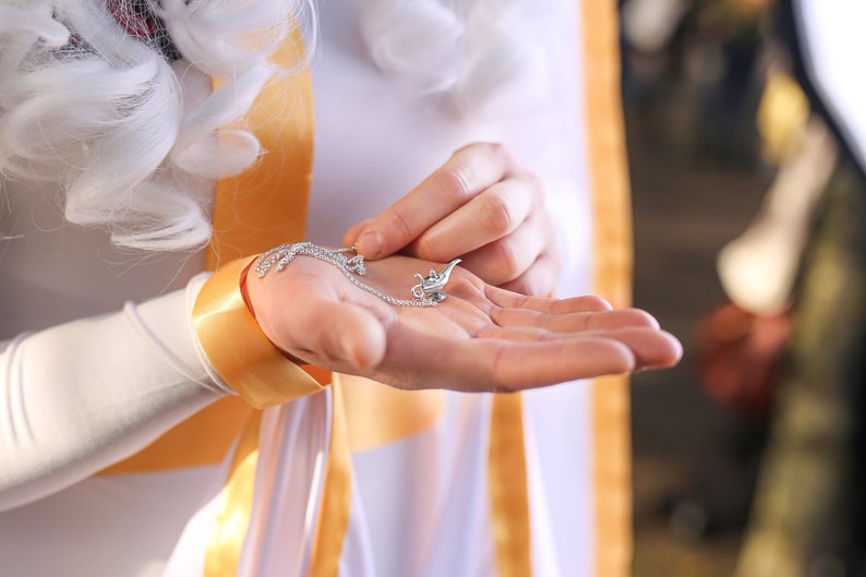 May include: A silver genie lamp charm on a silver chain necklace. The charm is detailed with a genie coming out of the lamp.