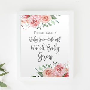 May include: A white framed sign with the text "PLEASE TAKE A Baby Succulent and Watch Baby Grow" in elegant script. The sign is decorated with watercolor roses in shades of pink and green. A sprig of greenery is placed to the left.
