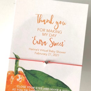 May include: A white card with orange text that reads "Thank you for making my day Extra Sweet." A red string bracelet with a small heart charm is attached. An orange and green watercolor illustration is on the card.