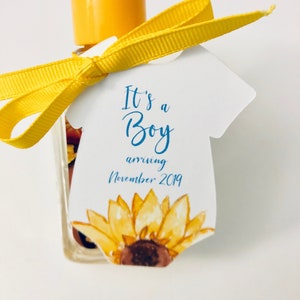 May include: A clear bottle with a yellow cap and a yellow ribbon tied around it. A white tag in the shape of a baby onesie is attached, featuring a watercolor sunflower and the text "It's a Boy arriving November 2019."