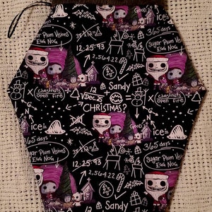 May include: A black stocking with a brown cuff features a repeating pattern of white illustrations of Jack Skellington and other characters from the Nightmare Before Christmas. The illustrations include equations and text such as "12.25.93", "Sandy", "Chestnuts open fire", and "Sugar Plum Visions Egg Nog".