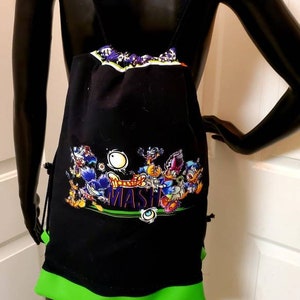 Puede incluir: Mochila negra con cordón, adornada con un gráfico de dibujos animados y la palabra "MASHER". La mochila tiene un ribete verde neón en la parte inferior y correas. La parte superior de la bolsa tiene un diseño estampado colorido.