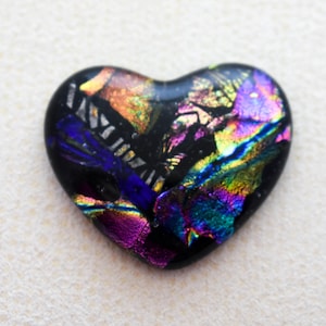 May include: A dichroic glass heart pendant with a black base and iridescent colors. The heart-shaped pendant features vibrant hues of purple, blue, green, and gold, creating a shimmering effect. The pendant is a unique piece of jewelry.