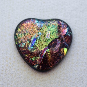 May include: A dichroic glass heart pendant with a dark border. The heart features a vibrant, iridescent pattern of green, blue, orange, and purple hues. The glass has a textured appearance, creating a unique, eye-catching design.