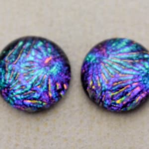 May include: Two circular glass cabochons featuring a vibrant dichroic pattern with iridescent swirls of deep purple, electric blue, and bright green. The surface of each piece is smooth and reflective, displaying a complex, multi-colored texture.