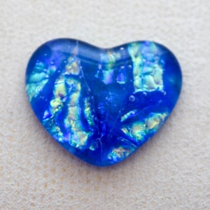 May include: A dichroic glass heart pendant in shades of blue and iridescent green. The heart-shaped pendant has a glossy finish and a textured, fractured appearance. The glass reflects light, creating a shimmering effect.