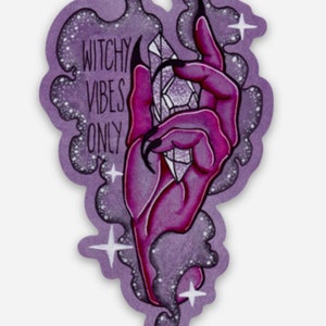 May include: A purple and pink hand with long, sharp nails holds a large, clear crystal. The hand is surrounded by a purple and white smoky cloud with white stars. The text "Witchy Vibes Only" is written in black on the cloud.