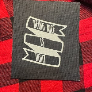 May include: Black and white iron-on patch with the text "Being Nice Is Tight" in a banner design.