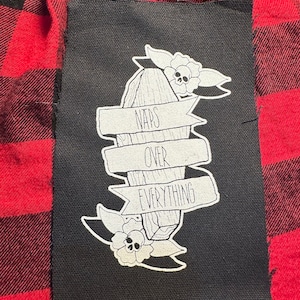 May include: Black and white iron-on patch with a coffin and floral design. The text on the patch reads "Naps Over Everything".