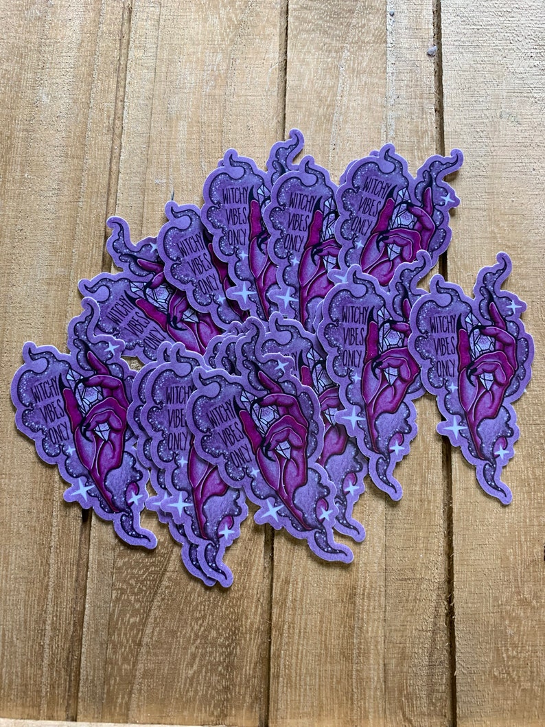 May include: A stack of purple and pink stickers with a hand holding a crystal and the text "Witchy Vibes Only" on each sticker.
