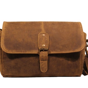 Puede incluir: Una bolsa de cámara de cuero marrón con cierre de solapa y hebilla. La bolsa tiene una correa larga ajustable y una hebilla de latón.