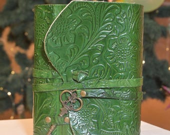 Könnte beinhalten: Ein grünes Lederjournal mit einem geprägten Blumenmuster und einem Schlüsselanhänger. Das Journal hat einen dekorativen Riemen und Metallakzente.