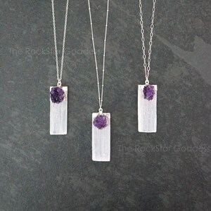 May include: Three silver necklaces with selenite crystal pendants and amethyst crystal accents. The necklaces are on a dark gray background.