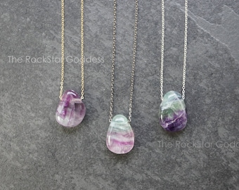 May include: Three necklaces with different colored chains and fluorite pendants. The fluorite pendants are all a teardrop shape and have shades of green, purple, and white.