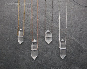 May include: Four necklaces with clear quartz crystal pendants on different colored chains. The chains are gold, rose gold, black, and silver.