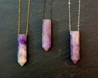 May include: Three amethyst crystal point necklaces with different chain styles: gold, silver, and black. Each necklace features a purple and white crystal point pendant.