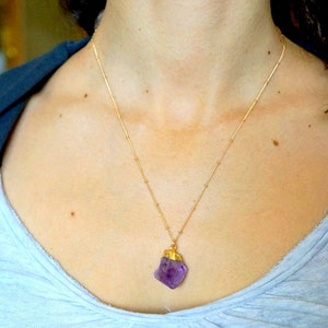 May include: A gold chain necklace with a large, raw amethyst pendant. The amethyst is a deep purple colour and has a natural, irregular shape.