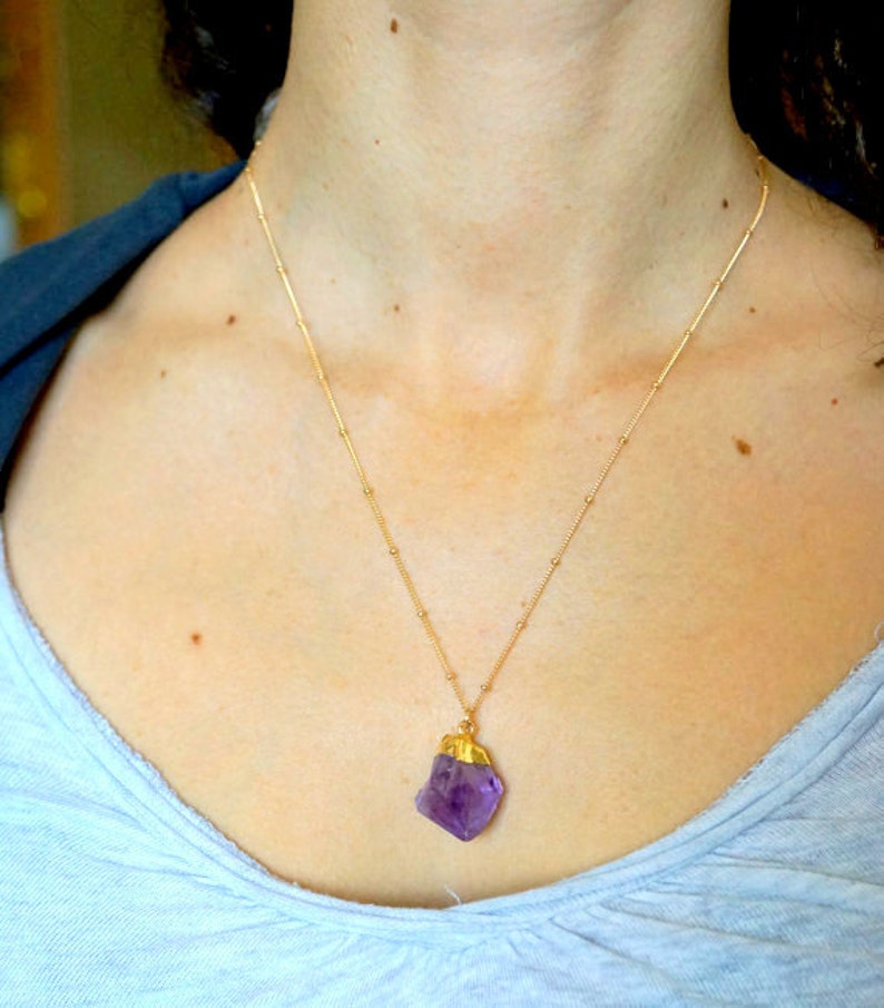 May include: A gold chain necklace with a large, raw amethyst pendant. The amethyst is a deep purple colour and has a natural, irregular shape.