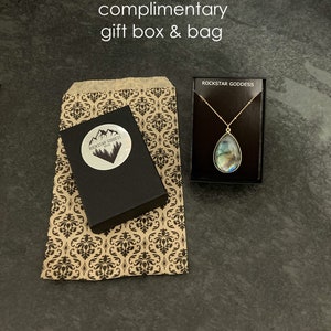 May include: A brown paper gift bag with a black and white damask pattern. The bag is next to a black gift box with a white sticker that says "Rockstar Goddess Jewelry".  A small black box with a gold chain necklace and a blue iridescent pendant is also shown. The box has the text "Rockstar Goddess" printed on the top.