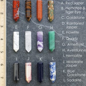 May include: Twelve different types of polished stones, each in the shape of a pointed obelisk, are arranged in rows of four. The stones are labeled with letters A through L, and the names of the stones are listed below the image. The stones are approximately 1.5 inches long.