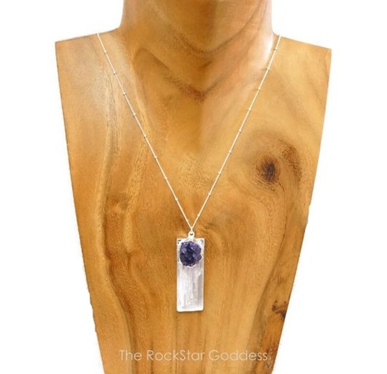 May include: A silver chain necklace with a rectangular pendant featuring a clear selenite crystal and a purple amethyst stone.