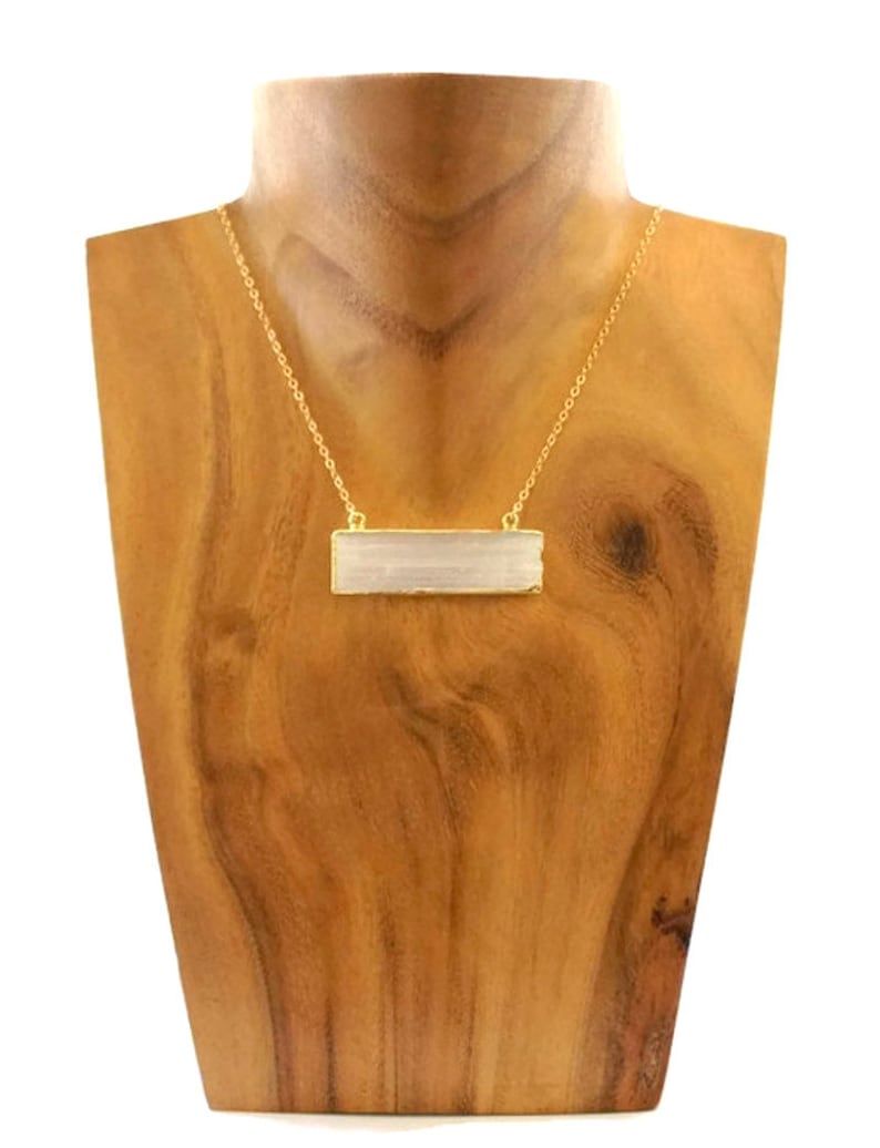 Pode incluir: Um colar de corrente de ouro com um pingente retangular de cristal de selenite. O pingente &eacute; de um branco claro transl&uacute;cido com um padr&atilde;o estriado.