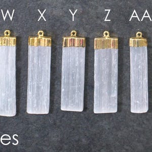 Op de afbeelding: Zes rechthoekige seleniet hangers met goudkleurige doppen worden getoond. De hangers zijn lichtblauw en staan naast twee munten. Het woord "inches" staat eronder gedrukt. De hangers zijn ongeveer 3,8 cm tot 5,1 cm lang.