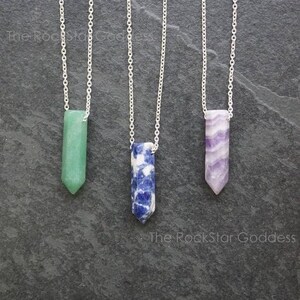 May include: Three silver necklaces with different colored crystal pendants. The pendants are all long and pointed, and they are made of green, blue, and purple crystals.