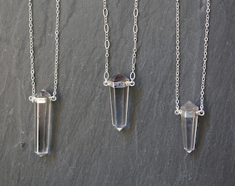 May include: Three silver chain necklaces with clear quartz crystal pendants. The pendants are faceted and have a hexagonal shape at the top. The chains are delicate and have a simple design.