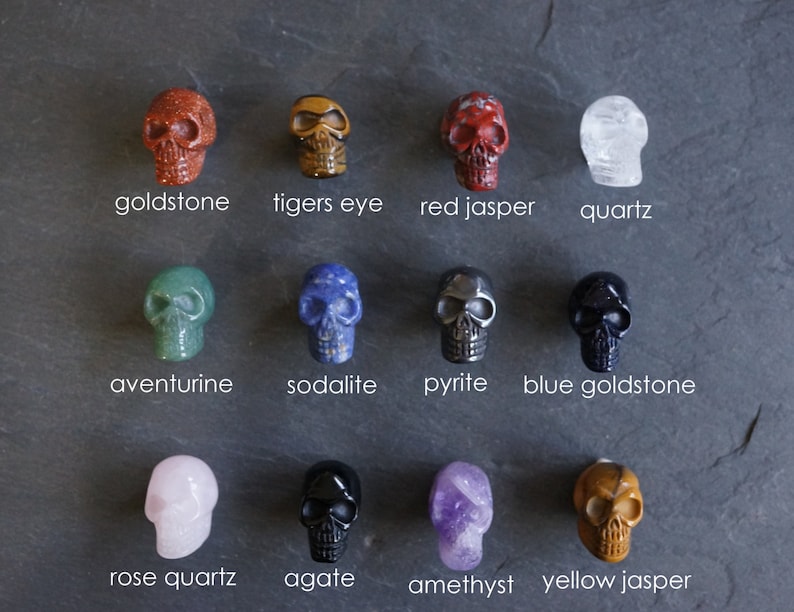 May include: Twelve different crystal skull figurines, each with a unique color and stone type. The stones include goldstone, tigers eye, red jasper, quartz, aventurine, sodalite, pyrite, blue goldstone, rose quartz, agate, amethyst, and yellow jasper.