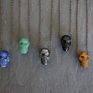 May include: Five silver chains with skull pendants made of different colored stones. The stones are blue, green, black, and brown.